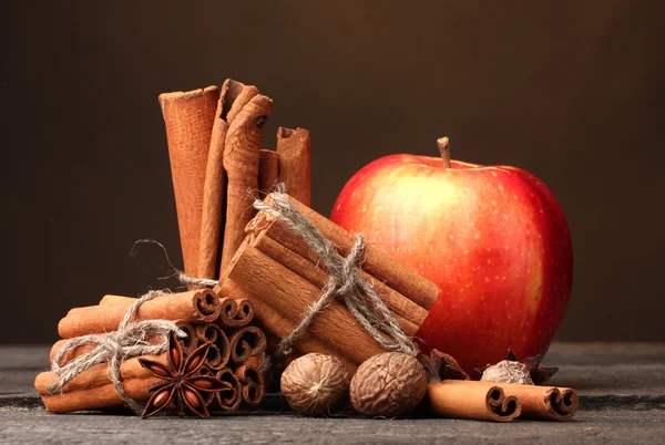 Kanelstänger, rött äpple, muskot och anis på träbord på brun bakgrunds — Stockfoto