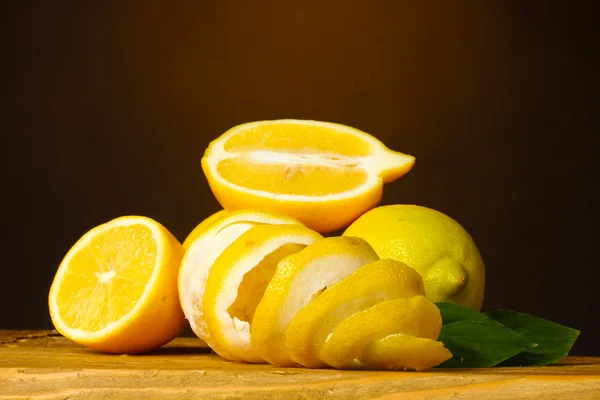Limoni maturi con foglie su tavolo di legno su sfondo marrone — Foto Stock