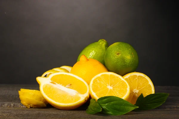 Спелые лимоны и лаймы с листьями на деревянном столе на сером фоне — стоковое фото