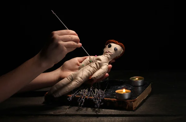 Voodoo panenku dívka propíchnout jehlou na dřevěný stůl ve světle svíček — Stock fotografie