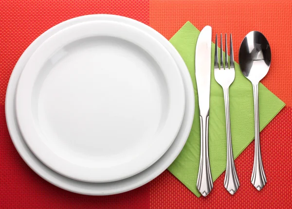 Біла порожня тарілка з виделкою, ложкою та ножем на червоній скатертині — стокове фото