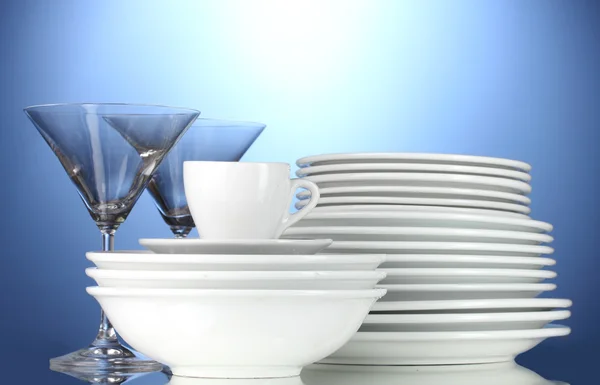 Tomma skålar, tallrikar, muggar och glas på blå bakgrund — Stockfoto