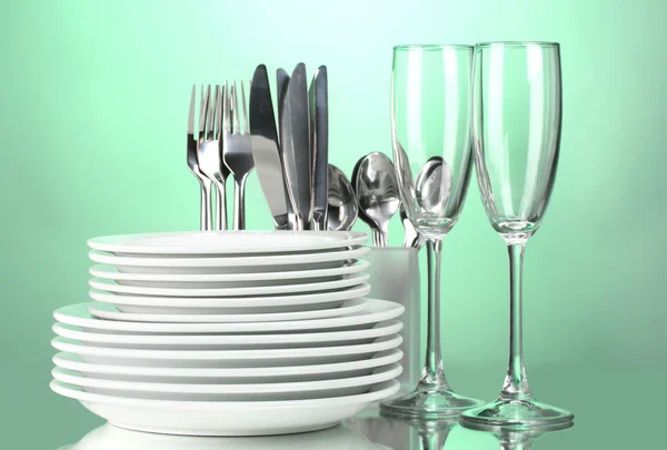 Clean plates, glasses and cutlery on green background — Stock Photo, Image