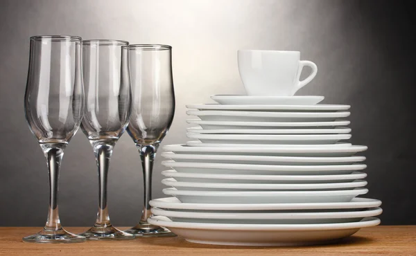 Clean plates, glasses and cup on wooden table on grey background — Stock Photo, Image