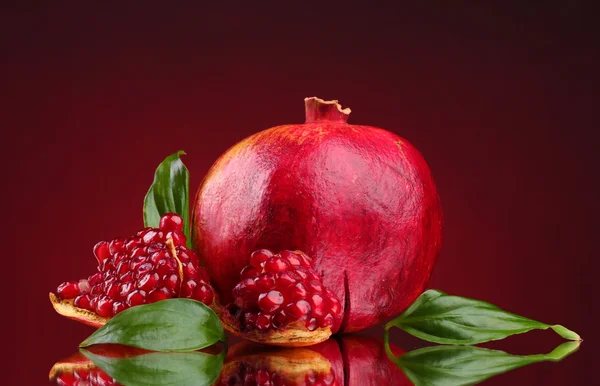 Ripe pomegranate fruit with leaves on red background — Stock Photo, Image