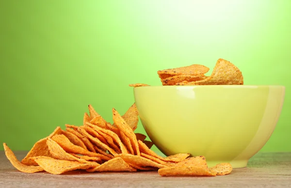 Tasty potato chips in green bowl on wooden table on green background — Stock Photo, Image