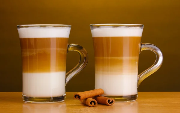 Fragrant сoffee latte in glass cups and cinnamon on wooden table on brown b — Stock Photo, Image