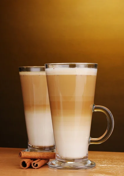 Fragante café con leche en taza de vidrio y canela en mesa de madera en ba marrón — Foto de Stock