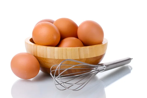 Metal whisk for whipping eggs and brown eggs in wooden bowl isolated on whi — Stock Photo, Image