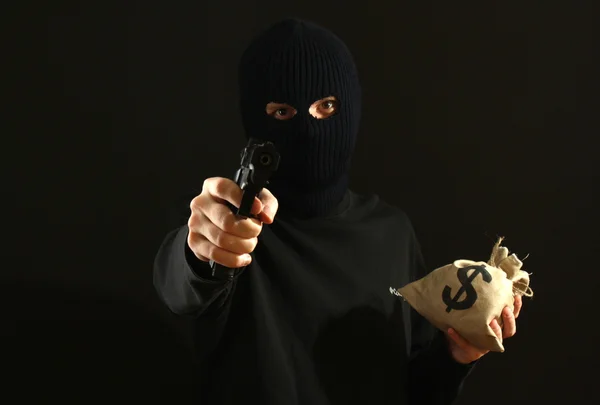 Bandido em máscara preta com arma e dinheiro isolado em preto — Fotografia de Stock