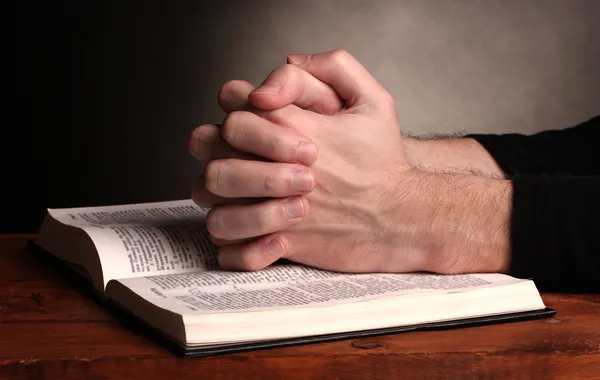 Hands folded in prayer over a Holy bible on wooden table on grey background — Stock Photo, Image