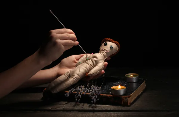 Menina boneca Voodoo perfurado por uma agulha em uma mesa de madeira à luz das velas Imagem De Stock