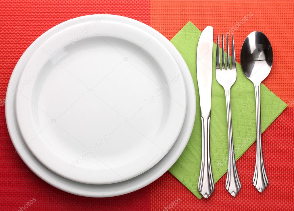 White empty plate with fork, spoon and knife on a red tablecloth