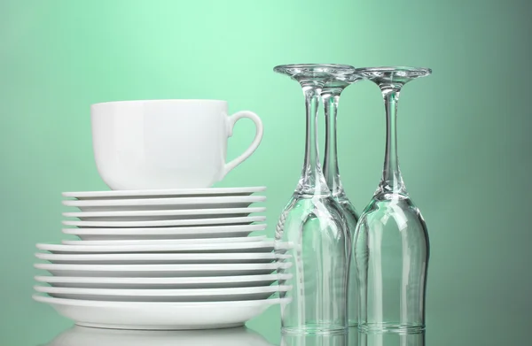 Clean plates, cup and glasses on green background — Stock Photo, Image