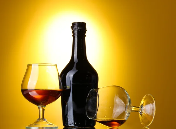 Óculos de conhaque e garrafa sobre fundo amarelo — Fotografia de Stock