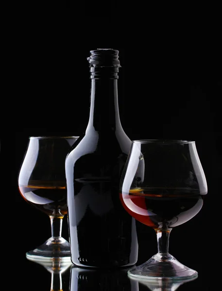 Vasos de brandy y botella sobre fondo negro —  Fotos de Stock