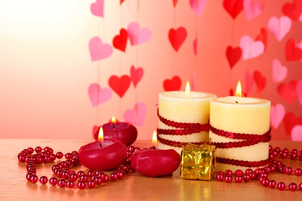 Belle candele con arredamento romantico su un tavolo di legno su sfondo rosso — Foto Stock