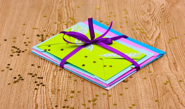 Група кольорових конвертів зі стрічкою та конфетті на дерев'яному фоні — стокове фото
