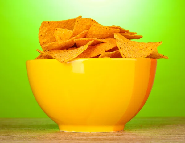 Вкусные картофельные чипсы в желтой миске на деревянном столе на зеленом фоне — стоковое фото