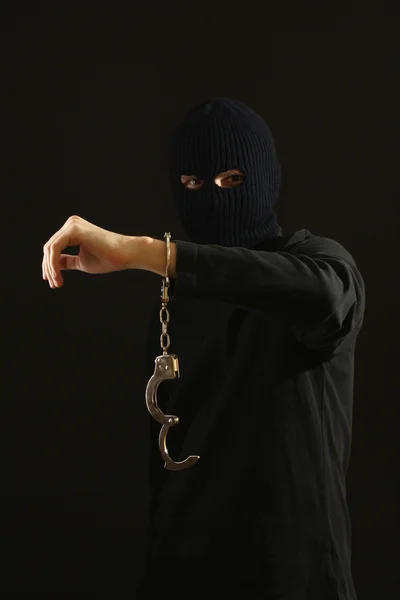 Bandido em máscara preta com algemas isoladas em preto — Fotografia de Stock