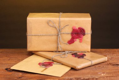 Parcels and envelope with sealing wax on wooden table on brown background clipart