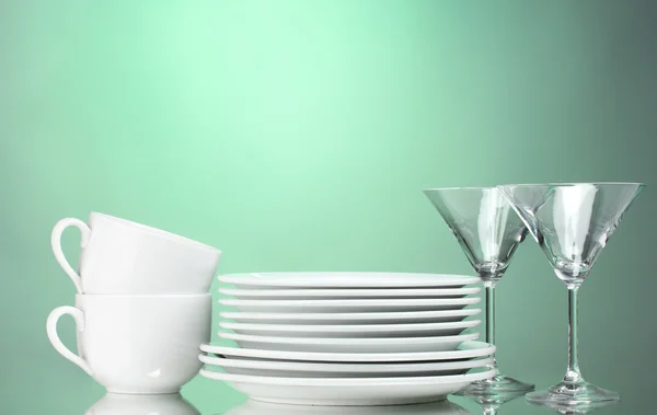 Clean plates, cups and glasses on green background — Stock Photo, Image