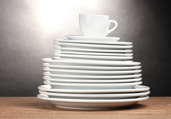 Чистые тарелки и чашки на деревянном столе на сером фоне — стоковое фото