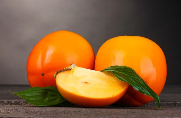 stock image Appetizing persimmons on wooden table on grey background