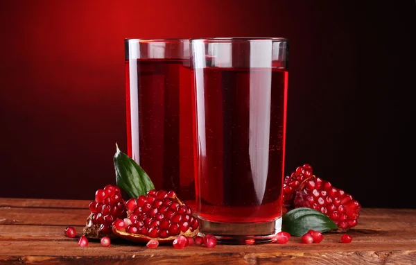 stock image Ripe pomergranate and glasses of juice on wooden table on red background