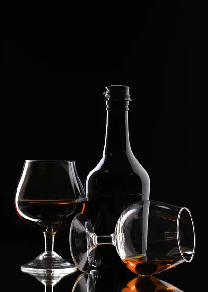 Glazen van brandy en fles op zwarte achtergrond — Stockfoto