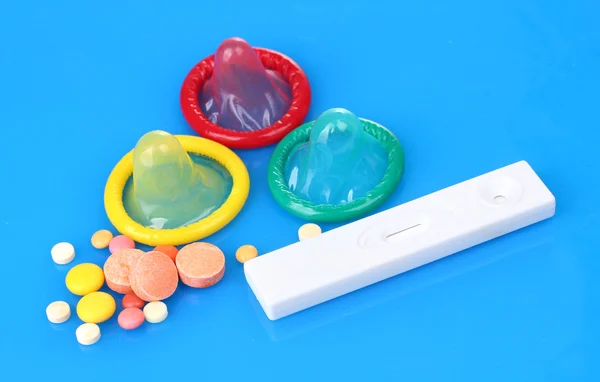 Geboorte condooms, zwangerschapstest en pillen op blauwe achtergrond — Stockfoto
