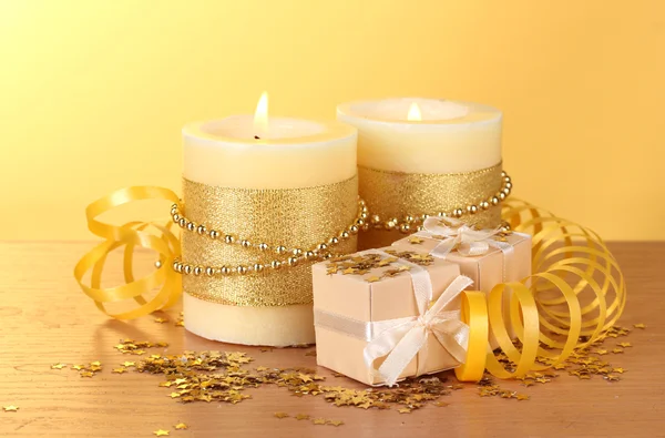 Schöne Kerzen und Geschenke auf Holztisch auf gelbem Hintergrund — Stockfoto