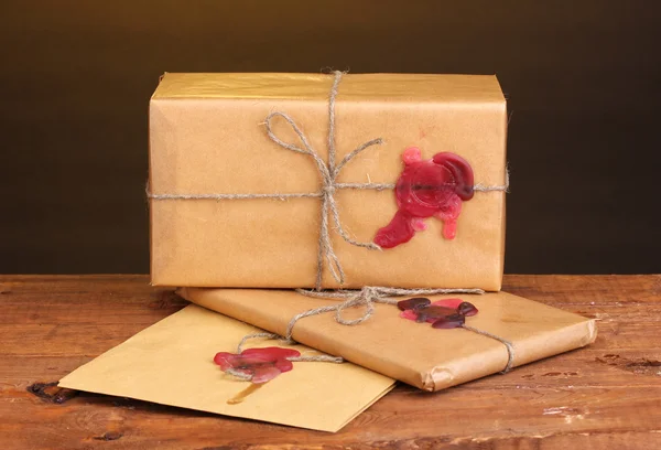 Посылки и конверт с герметичным воском на деревянном столе на коричневом фоне — стоковое фото