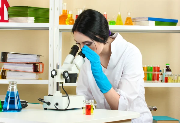 看着显微镜在化学实验室中的年轻女科学家 — 图库照片