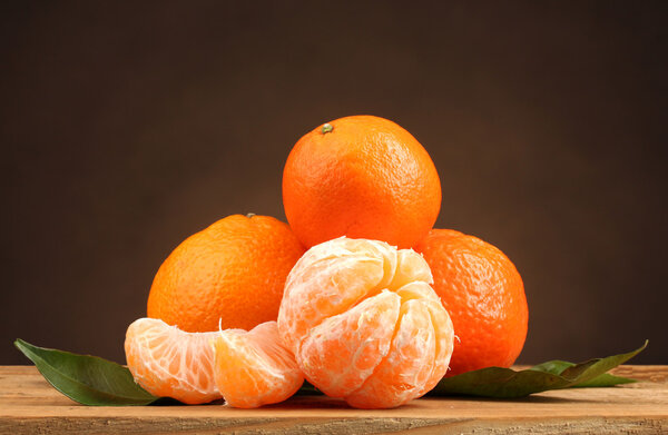 Tangerines with leaves on wooden table on brown background