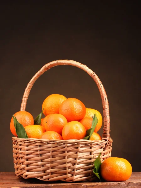 Mandarinky s listy v krásné koše na dřevěný stůl na hnědé pozadí — Stock fotografie