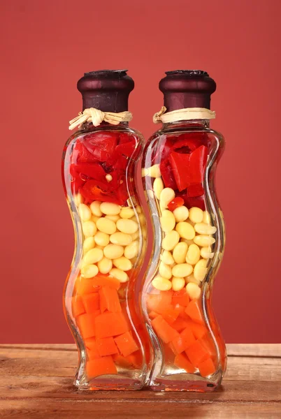 Due bottiglie con peperone rosso, fagioli, carote per arredo cucina su dorso rosso — Foto Stock