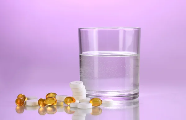 Glas Wasser und Pillen auf violettem Hintergrund — Stockfoto