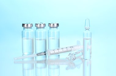 Syringe and medical ampoules on blue background clipart