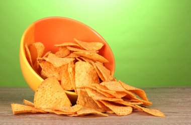 Tasty potato chips in yellow bowl on wooden table on green background clipart