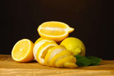 Ripe lemons with leaves on wooden table on brown background clipart