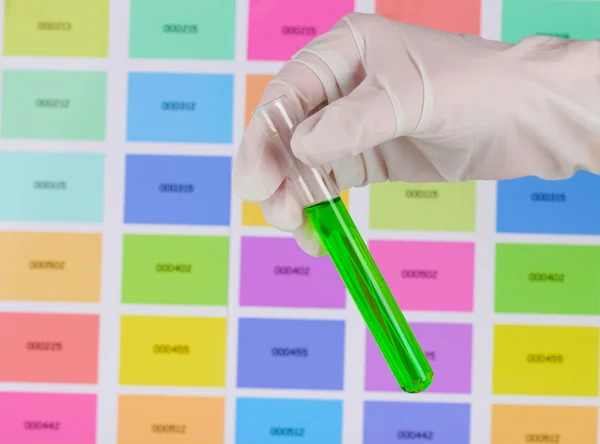 Rura z zielonej cieczy w dłoni na tle próbek kolorów — Zdjęcie stockowe