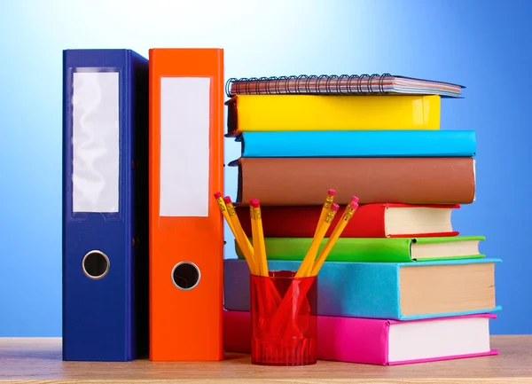 Carpetas de oficina brillantes y libros con papelería en mesa de madera en bac azul — Foto de Stock