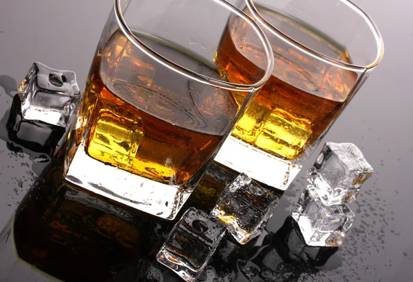 Two glasses of scotch whiskey and ice on grey table