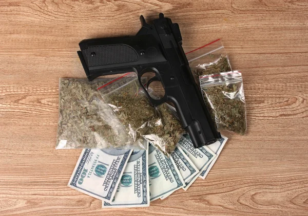 Marihuana in pakketten, dollars en pistool op houten achtergrond — Stockfoto