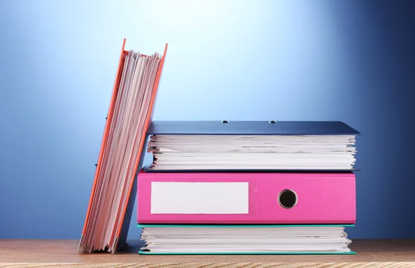 Яркие офисные папки на деревянном столе на синем фоне — стоковое фото