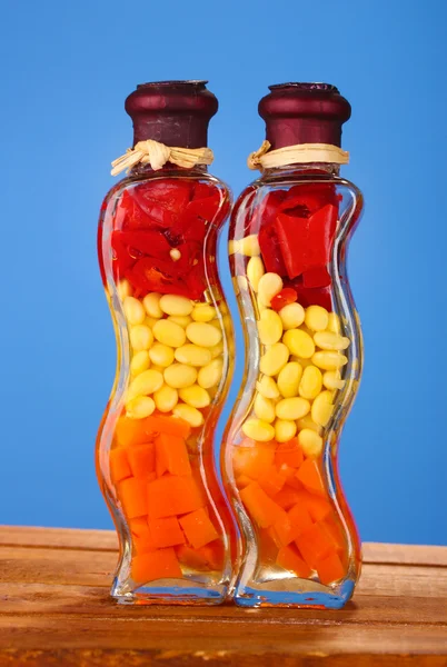 Due bottiglie con pepe rosso, fagioli, carote per l'arredamento della cucina su dorso blu — Foto Stock