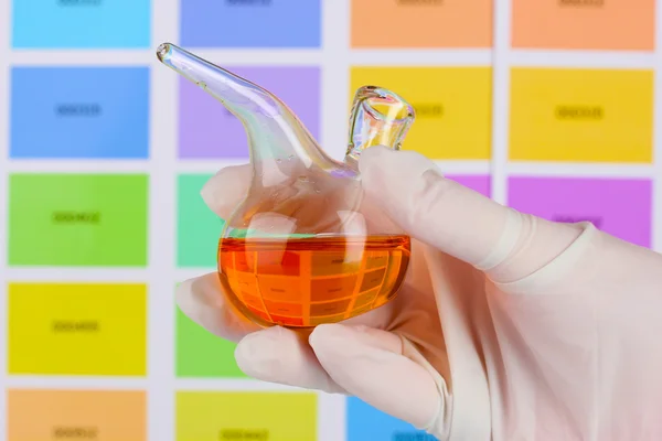 Flask with orange liquid in hand on color samples background — Stock Photo, Image