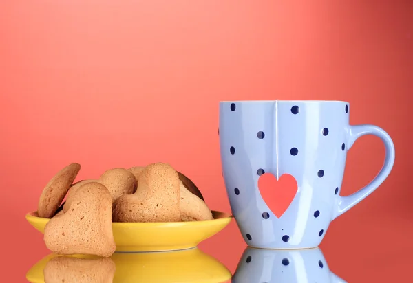 Hjärtformade kakor på gula plattan och cup med tepåse på röd bakgrund — Stockfoto
