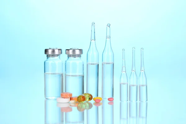 Injectiespuit met medische ampullen en tabletten op blauwe achtergrond — Stockfoto